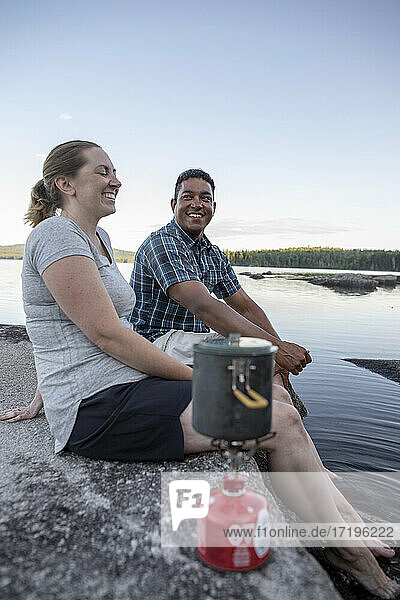 Afrikanischer Mann und weiße Frau lachen und lächeln beim Camping mit Kocher