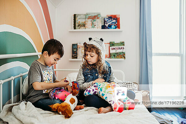 Brother and sister sitting on bed in rainbow kids room playing