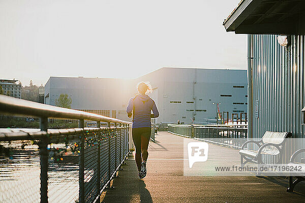 Frau läuft am frühen Morgen auf einem gepflasterten Weg in goldenes Licht