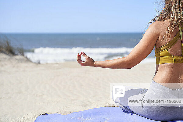 Nahaufnahme einer jungen Frau  die von hinten mit geschlossenen Fingern vor dem Meer eine meditative Geste macht.
