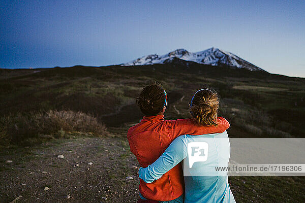 Zwei Freundinnen umarmen sich und blicken in der Abenddämmerung auf die Berge
