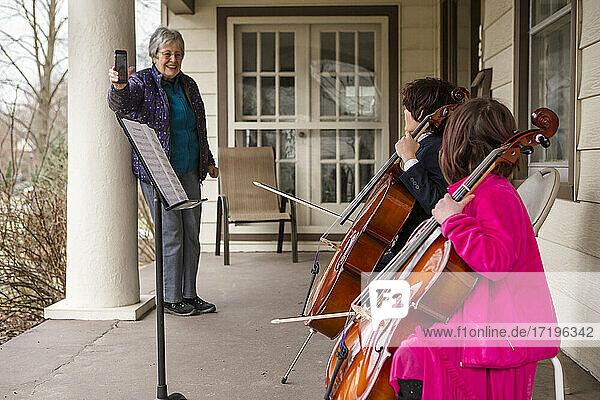 Eine ältere Frau nimmt zwei Kinder auf  die auf der Veranda ein Cellokonzert geben