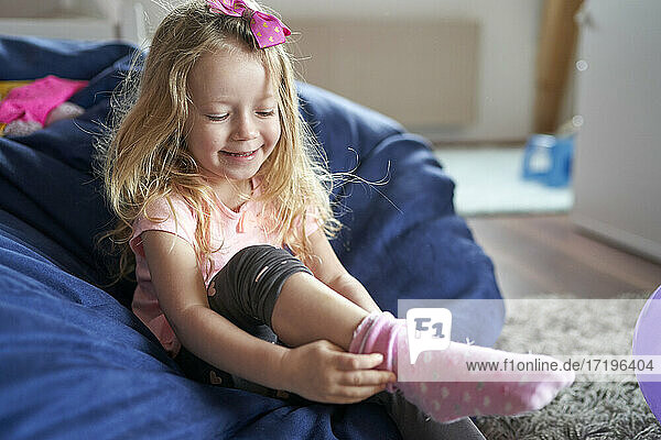 Glückliches kleines Mädchen  das im Sitzsack sitzt und seine rosa Socken anzieht