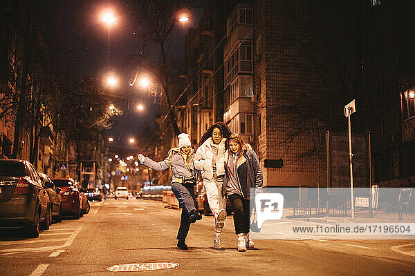 Glückliche weibliche Freunde haben Spaß auf der Straße in der Stadt in der Nacht zu Fuß