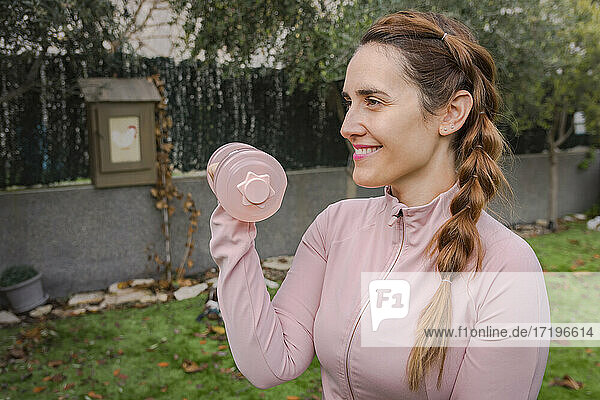 Lächelnde Frau in rosa gekleidet hebt Hantel  Fitness zu Hause