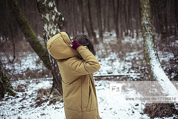 Person setzt Kapuze auf Wintermantel draußen im verschneiten Wald