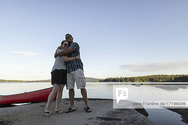 Couple hug and embrace on rocky lake shore in Maine with canoe
