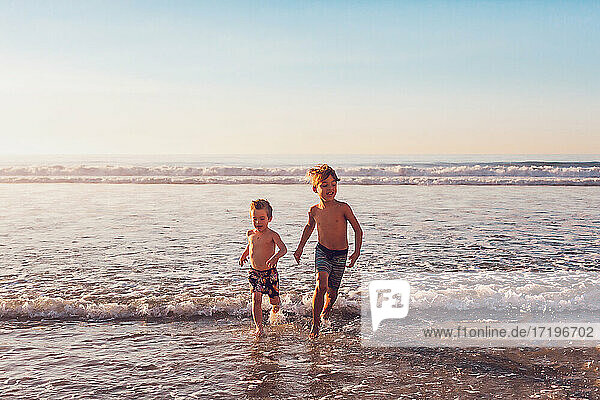 Two boys running in the water at the beach.