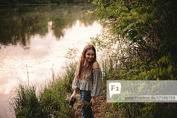 Happy teenage girl standing by river in forest during summer