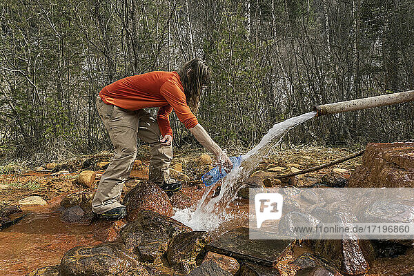 Side view of man filling bottle with water flowing through pipe in forest