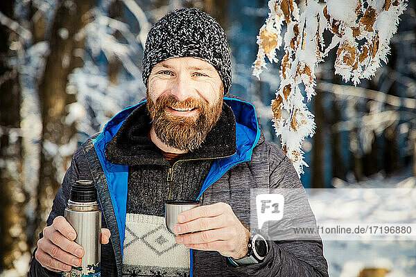 Mann trinkt heißen Tee im Winterwald