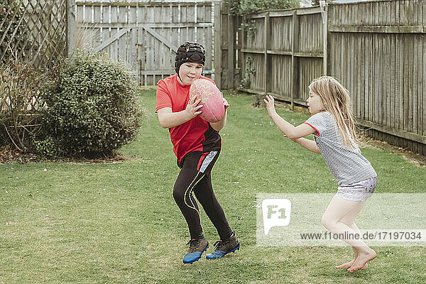 Junger Bruder und Schwester spielen mit Rugby-Ball im Hinterhof