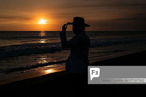 Silhouette eines Mannes mit Hut vor dem Meer bei Sonnenuntergang