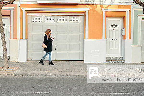 Frau geht auf der Straße  während sie auf ihr Smartphone schaut