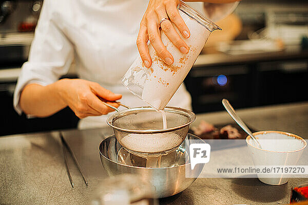 Köchin benutzt Sieb bei der Zubereitung einer Soße im Restaurant