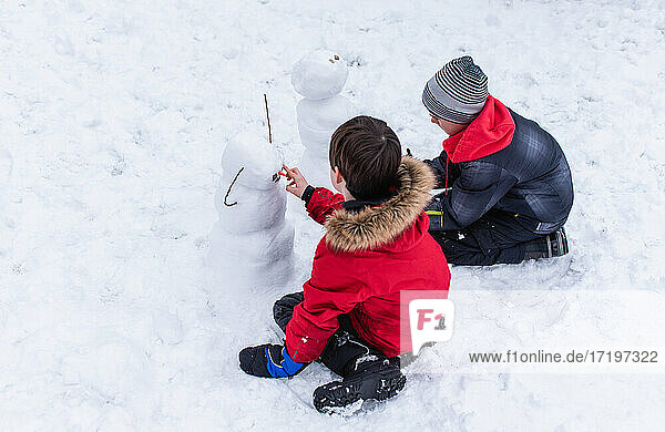 Zwei Jungen in Winterkleidung bauen an einem Wintertag Schneemänner.