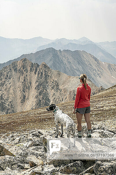 Rear view of female hiker with dog on mountain against sky during vacation