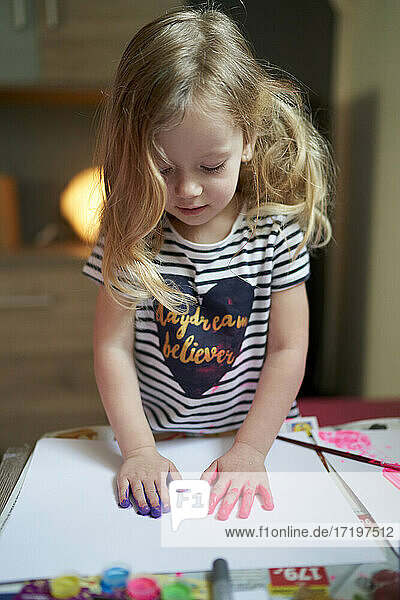 Niedliches kleines Mädchen  das gemalte Palmen auf ein weißes Blatt Papier legt.