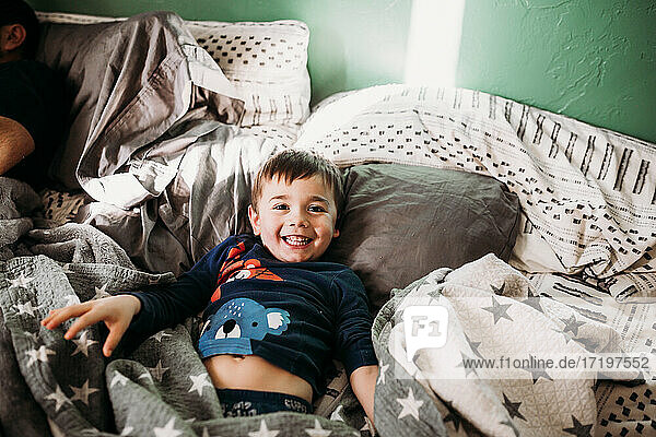 Junge im Schlafanzug im Bett lächelnd und in die Kamera schauend