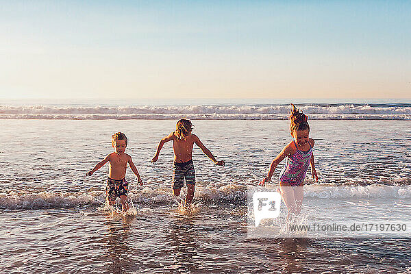 Drei kleine Kinder laufen im Wasser am Strand
