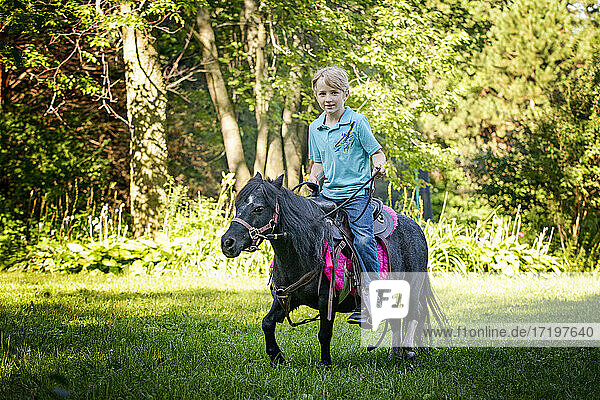 Der kleine Blonde reitet auf seinem kleinen schwarzen Pony durch die Landschaft.