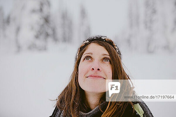 Junge Frau mit braunen Haaren und Augen blickt auf schneebedeckte Bäume