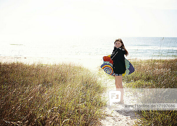 Red Haired Tween girl with boogie board on sand path to ocean.