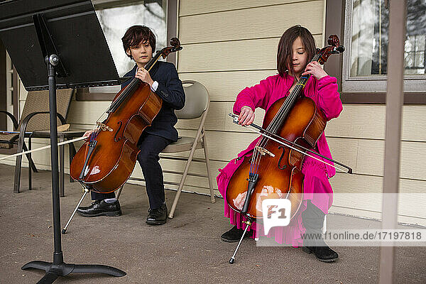 Ein Junge mit einem Cello schaut zu  während seine Schwester ihr Instrument spielt