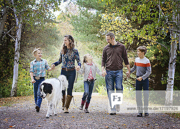 Glückliche fünfköpfige Familie  die mit ihrem großen Hund eine Landstraße entlangläuft.