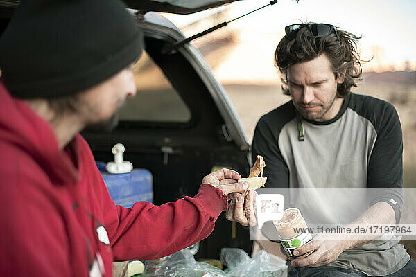 Männliche Freunde essen zusammen  während sie im Kofferraum eines Geländewagens im Canyonlands National Park sitzen