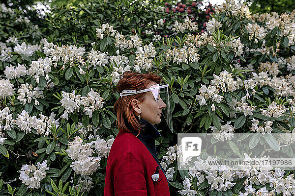 Frau mit Gesichtsschutz bei Pflanzen im Park während einer Pandemie