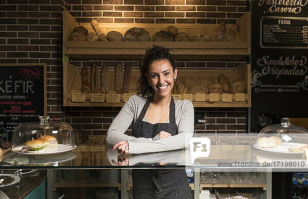 Lächelnde Frau steht vor einem Regal mit Backwaren in einer beleuchteten Bäckerei