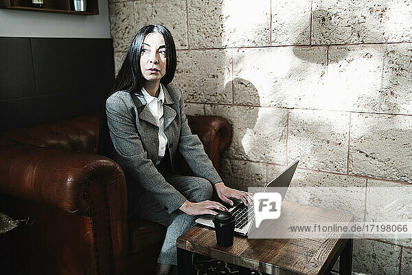 Seriöse Geschäftsfrau  die an einem Laptop arbeitet und wegschaut  während sie in einem Café sitzt