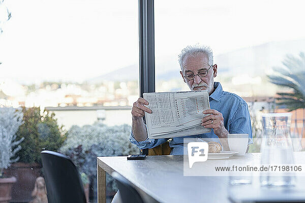 Älterer Mann liest Zeitung  während er zu Hause am Tisch sitzt