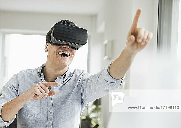 Cheerful male entrepreneur gesturing while wearing virtual reality simulator at home office