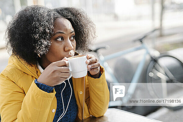 Junge Frau schaut weg  während sie in einem Straßencafé Kaffee trinkt