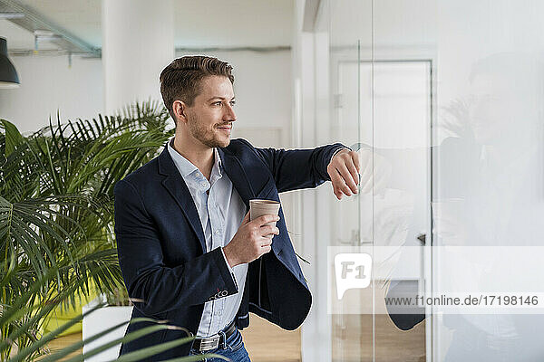 Hübscher Geschäftsmann Einweg-Kaffeetasse lehnt auf Glas im Büro
