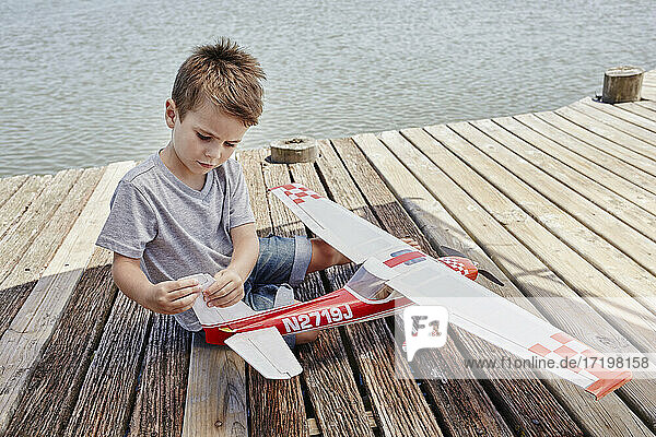 Junge überprüft Flugzeugspielzeug  während er auf dem Pier sitzt