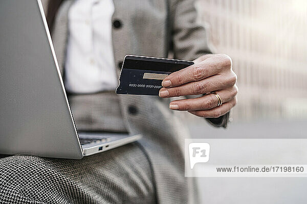 Geschäftsfrau mit Kreditkarte und Laptop im Freien sitzend