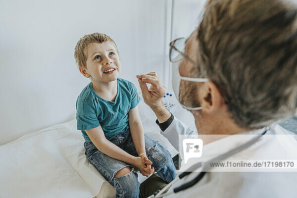 Doctor taking nasal swab test of boy while sitting at clinic