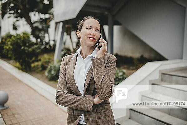 Businesswoman talking on smart phone while standing against building