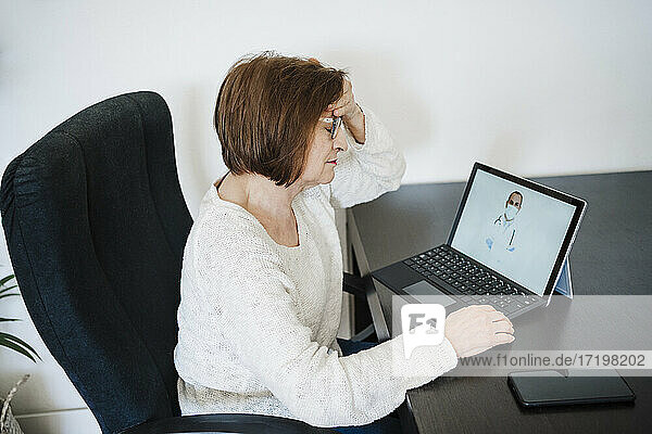 Frau  die unter Kopfschmerzen leidet  lässt sich von einem Arzt per Videoanruf über ihren Laptop zu Hause beraten
