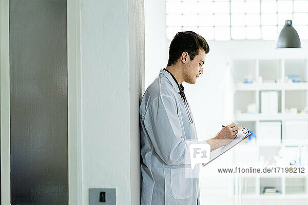 Männliche medizinische Fachkraft schreibt Notizen  während sie im Krankenhaus an der Wand steht