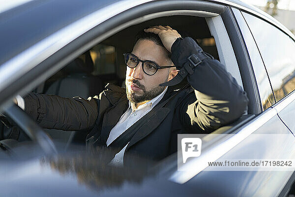 Male entrepreneur with hand in hair looking away while driving car