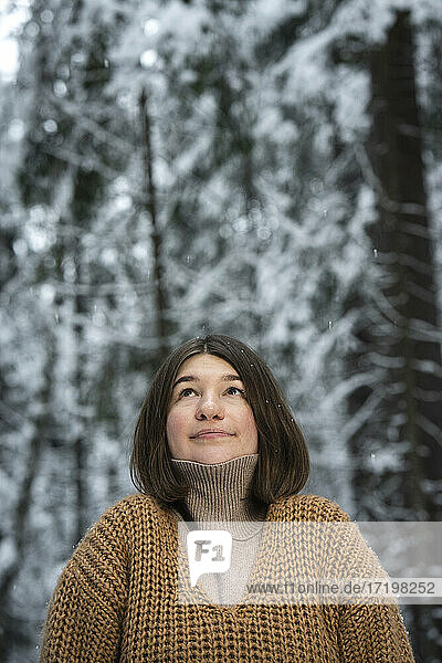 Junge Frau mit Pullover  die im Wald steht und nach oben schaut