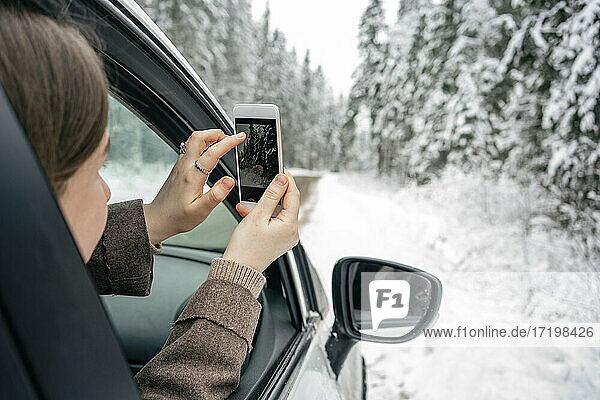 Woman photographing through mobile phone while sitting in car