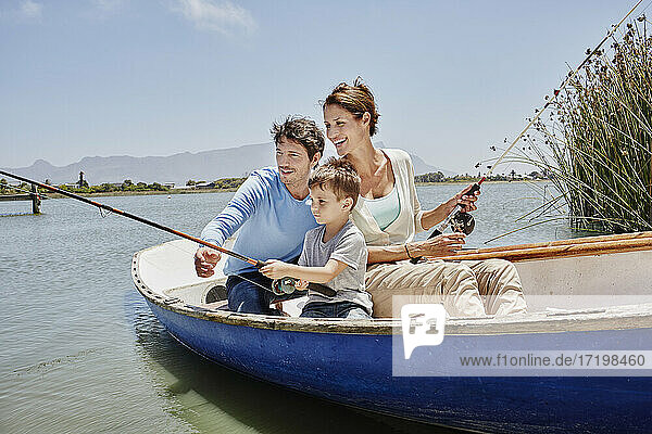 Eltern mit Angelrute sitzen neben dem Sohn im Ruderboot auf dem See