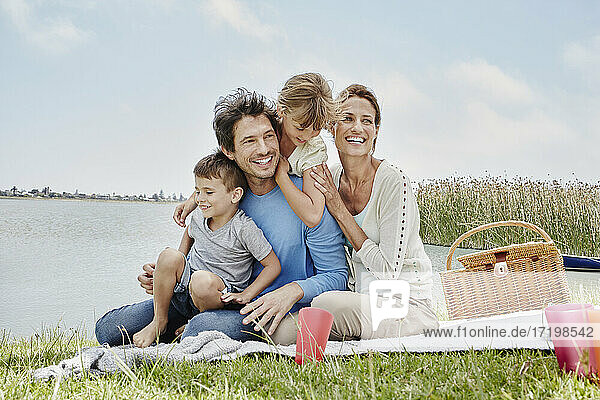 Glückliche Familie sitzt in einer Reihe auf einer Decke am See