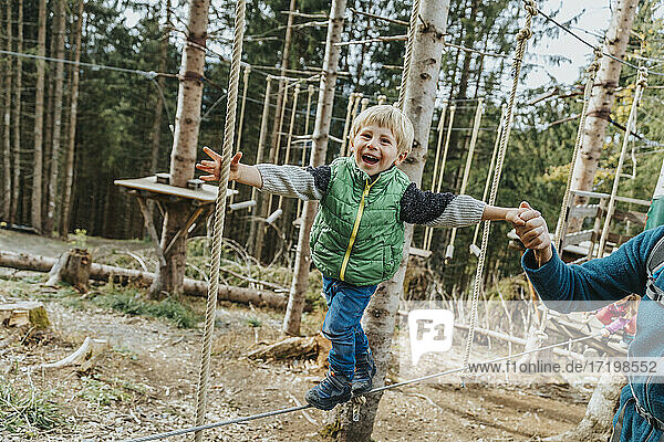 Verspielter Junge im Hochseilgarten  unterstützt von seinem Vater  im Wald im Salzburger Land  Österreich