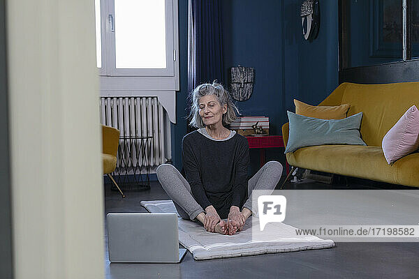 Senior woman doing yoga through online tutorial on laptop at home